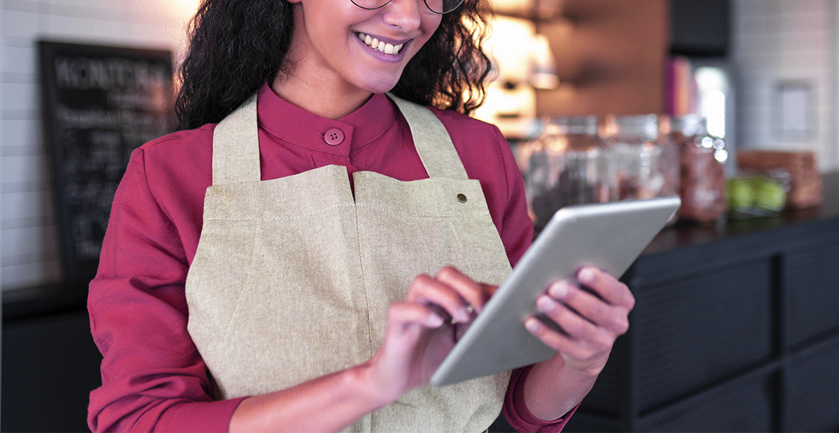 mulher de camisa rosa, sorrindo com um tablet na mão